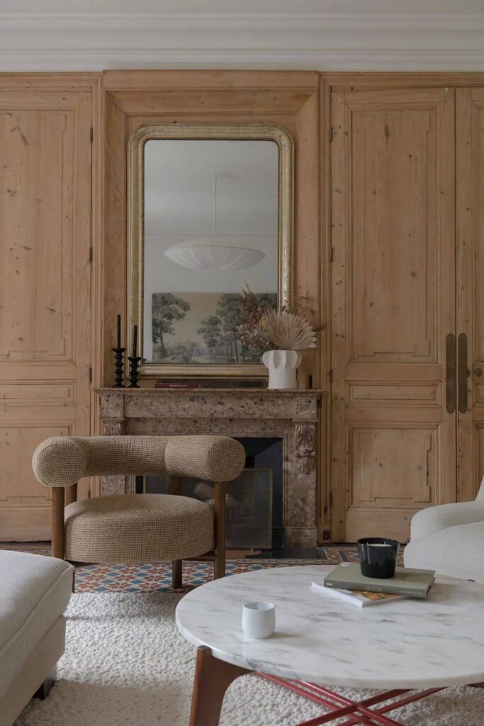 Salon à l'esprit vintage avec boiseries claires, cheminée en marbre, grand miroir ancien et table basse ronde.